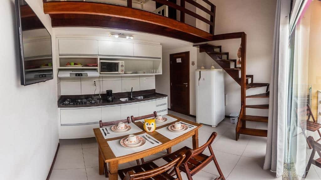 Cozinha do Para Vos y Porque Si. No fundo uma pia com utensílios da cozinha. Do lado esquerdo uma televisão, no meio uma mesa posta. Do lado direito uma escada. Foto para ilustrar post sobre airbnb em Morro de São Paulo.