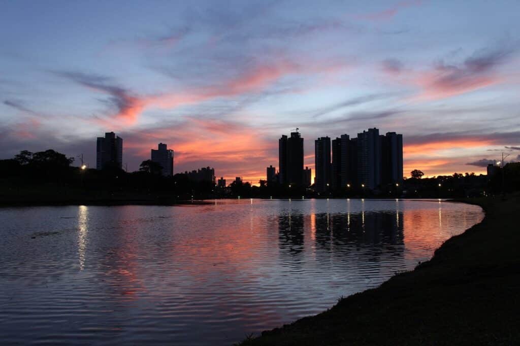 Parque com uma grande lago. Ao fundo há diversos prédios e árvores.