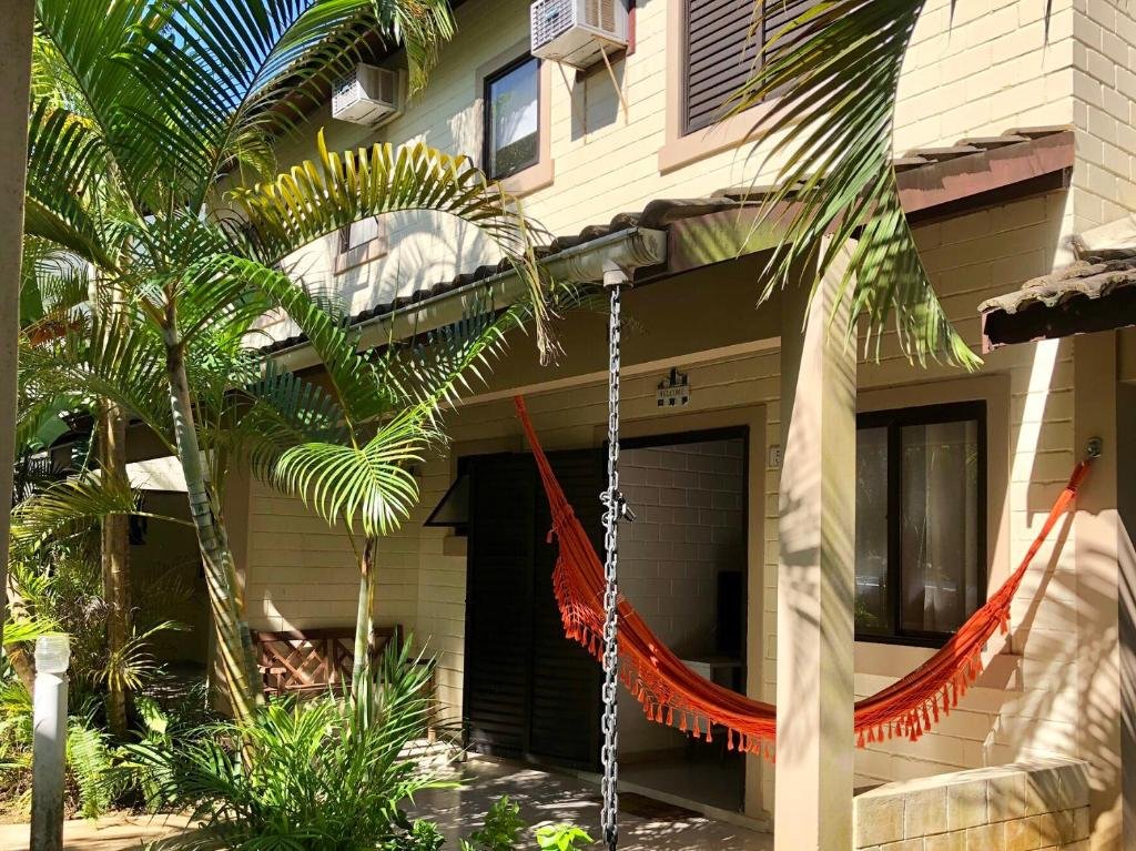 Exterior da Paúba Beach House. A casa tem dois andares, é feita de tijolos claros, há uma rede na varanda e coqueiros.