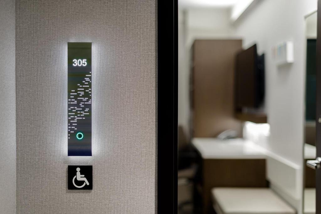 número do quarto 302 acompanhado por sinais de Braille, além de um símbolo de cadeirante abaixo. No lado direito da imagem é possível ver uma parte desfocada do quarto.
