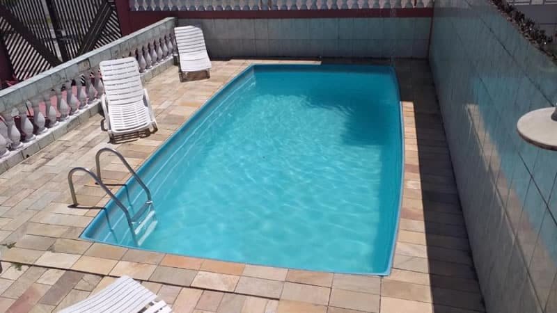 Piscina azul com escada de metal, duas espreguiçadeiras e paredes de azulejo branco em volta.