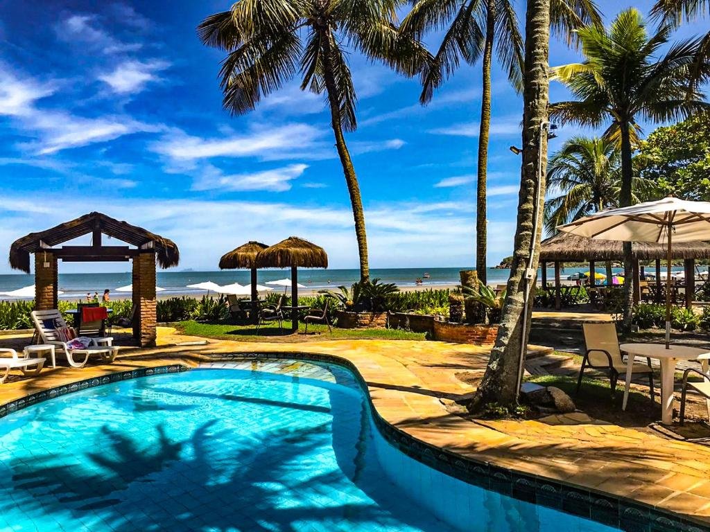 Vista da piscina do Barequeçaba Praia Hotel durante o dia com quiosques, coqueiros e ao fundo a praia. Representa pousadas na praia de Guaecá.