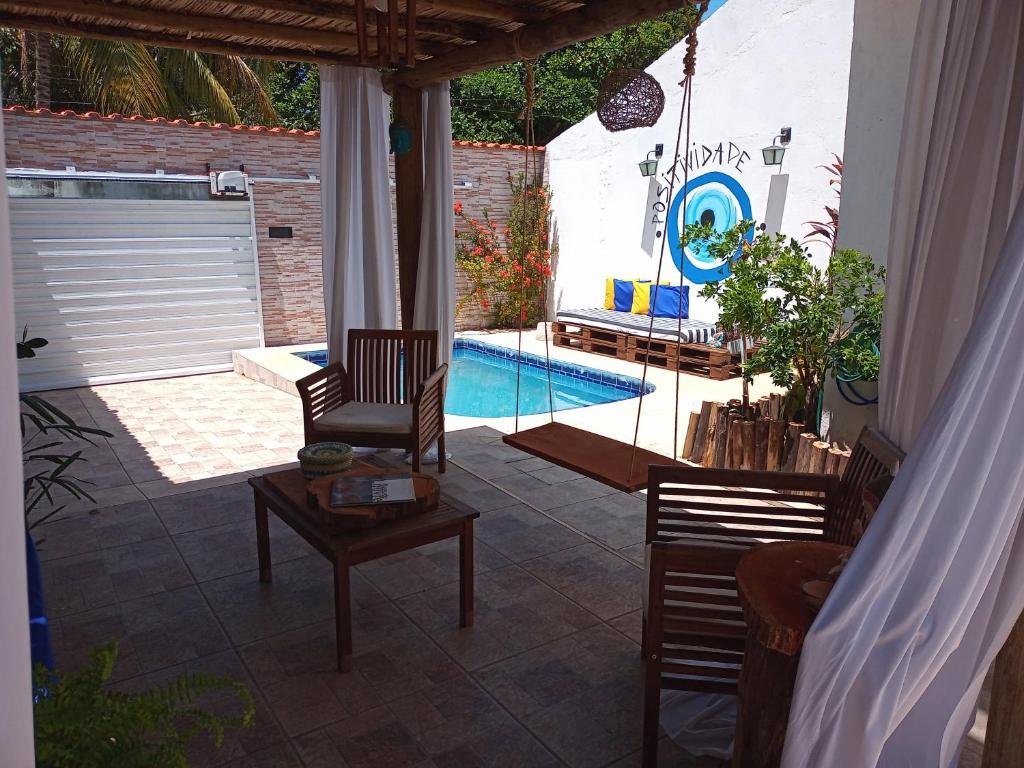 Área externa do Canto Pedra da Lua. Dois bancos de madeira, um balanço de madeira e uma mesa no centro. No fundo, uma piscina, um banco com almofadas e o portão.