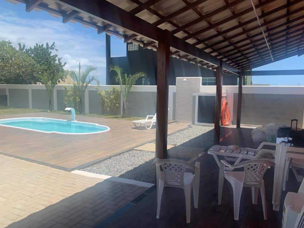 Área externa do airbnb Casa em condomínio fechado. No lado direito há uma área coberta com uma mesa de plástico e cadeiras. Já no lado esquerdo há uma área aberta bem espaço com uma piscina.