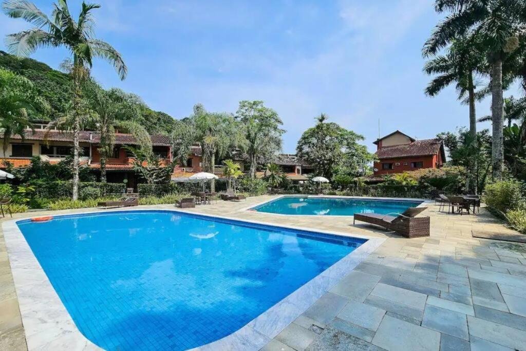 Piscina da Casa em Condomínio Pé na Areia na Praia do Engenho durante o dia com piscina do lado esquerdo da imagem a frente e do lado direito ao fundo outra piscina.
