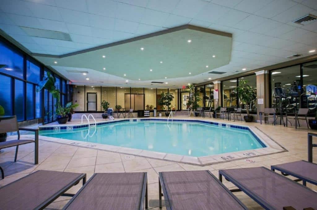 Imagem da piscina no Crowne Plaza Newark Airport. A piscina é espaçosa, com água cristalina e cercada por espreguiçadeiras. Há também guarda-sóis posicionados estrategicamente para fornecer sombra. O ambiente é convidativo e relaxante.