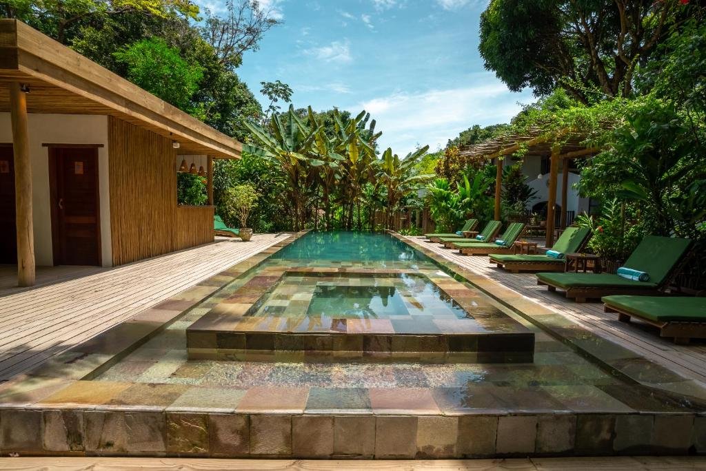 Piscina do Da Graça Hotel durante o dia com cadeiras com estofado verde do lado direito e ao fundo árvores. Representa resorts em Trancoso.
