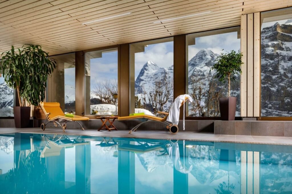 Piscina coberta do Eiger Mürren Swiss Quality Hotel com piscina a frente e ao fundo duas cadeiras.