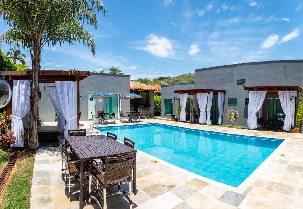 Piscina do Escarpas Eco Village, com alguns bangalôs espalhados pelo deck, além de cadeiras e mesas, com algumas árvores ao redor