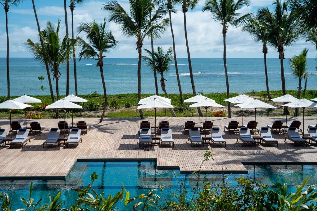 Vista de cima da piscina do Hotel Fasano Trancoso com cadeiras na beira da piscina com vista para o mar. Representa resorts em Trancoso.