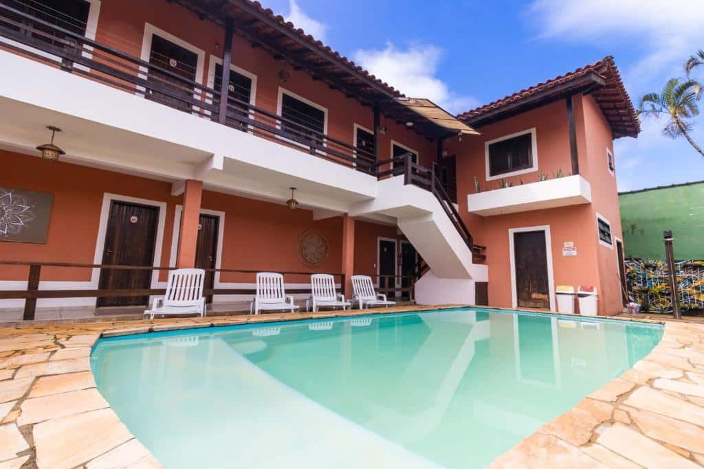 Piscina da HOTELARE Bóra Morá Pousada, com espreguiçadeiras ao redor da pousada pintada de vermelho com detalhes em branco