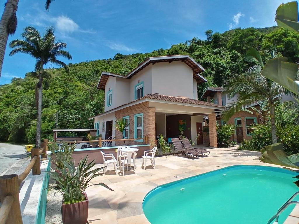 Vista da piscina do Kauano Pousada Barequeçaba durante o dia com cadeiras do lado esquerdo e ao fundo a hospedagem. Representa pousadas na praia de Guaecá.