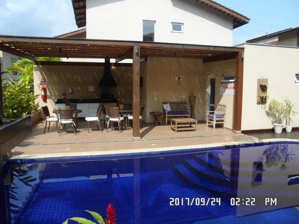 Frente da Linda Casa em Juquehy durante o dia com piscina em frente da imagem ao fundo a varanda com cadeiras e mesas e ao fundo a estadia.