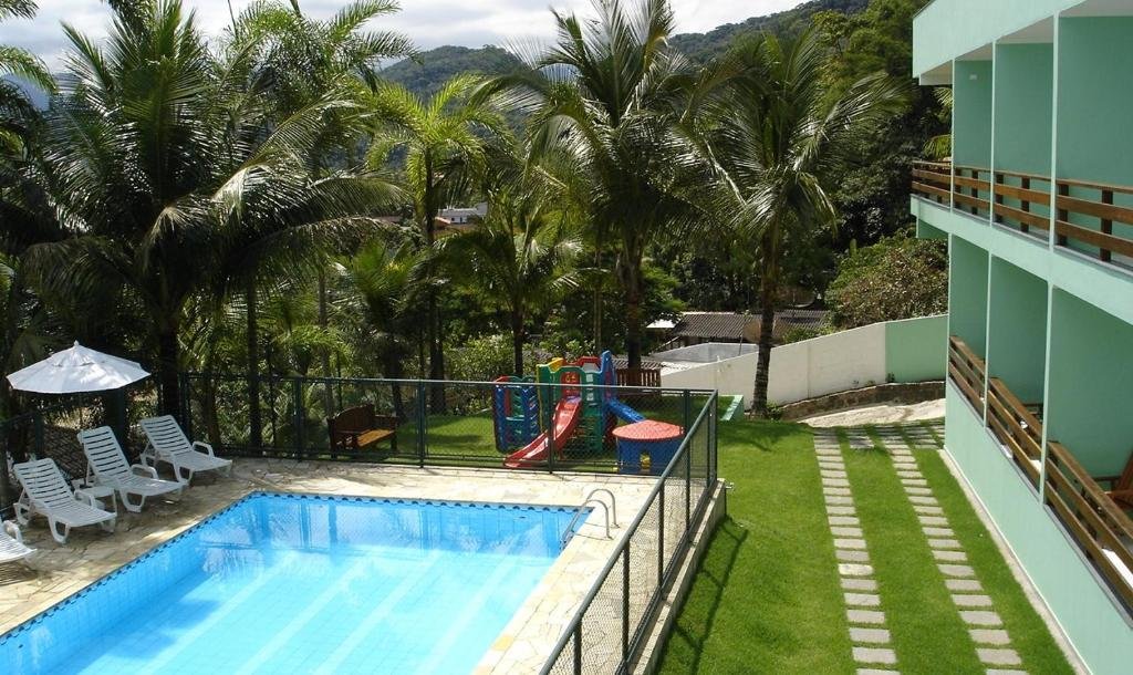 Piscina da Marencanto Pousada, uma piscina cercada, com espreguiçadeiras embaixo de grande coqueiros, do lado de fora, grama e um pequeno parquinho para crianças