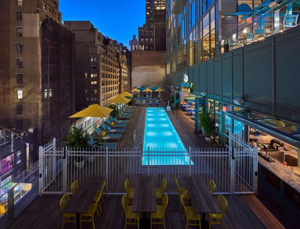 área da piscina no terraço do Margaritaville Resort Times Square com várias espreguiçadeiras ao redor da piscina retangular que conta com uma cadeira de banho para pessoas com deficiência motora.