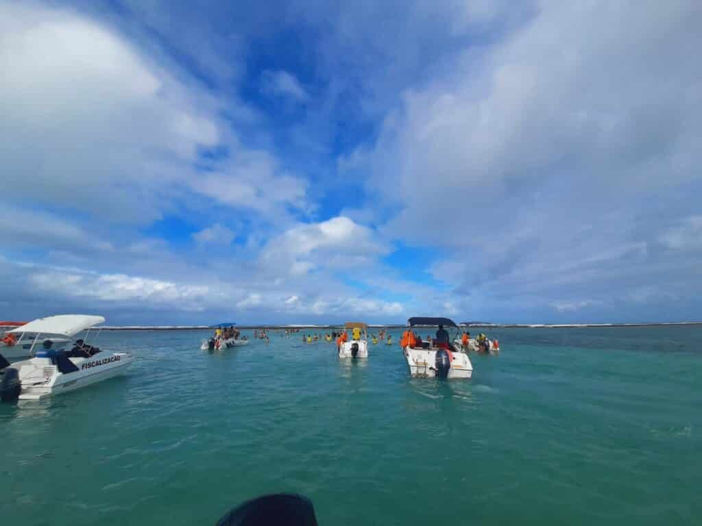 Mar verde turquesa com alguns barcos navegando. O local é a piscina natural Ponta do Mangue, em Maragogi