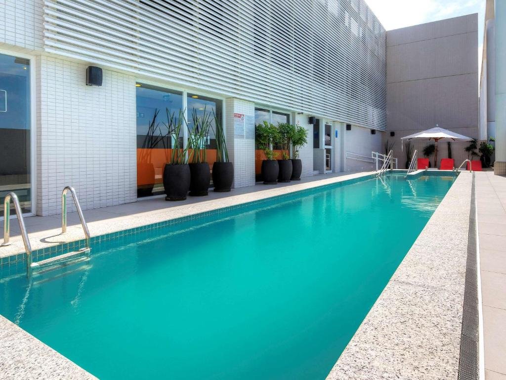 Piscina do Novotel Santos Gonzaga muito comprida e com algunas vasos de flores nas laterais