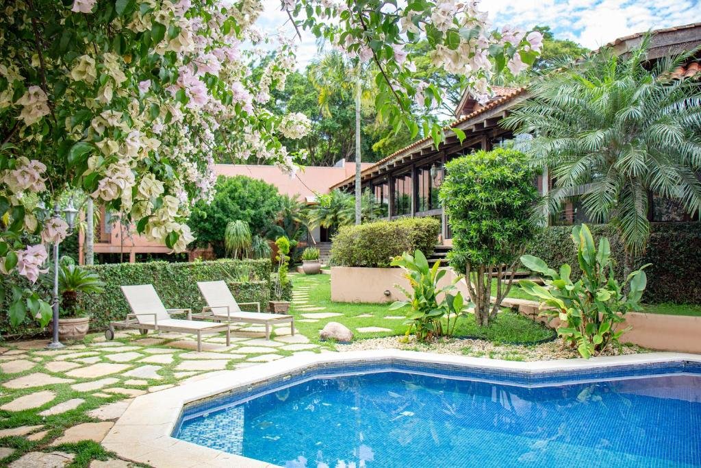 piscina da Pousada Casa da Quineira no jardim florido sob um céu nublado na Chapada dos Guimarães