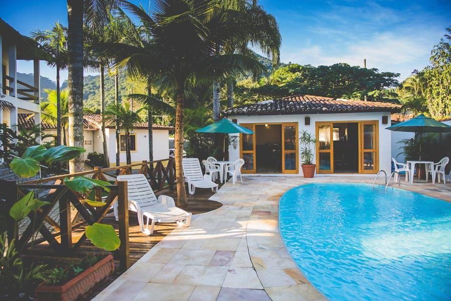 Área de lazer da Pousada Casarão com piscina do lado direito da imagem, do lado esquerdo cadeiras e ao fundo a estadia. Representa airbnb na praia de Calhetas