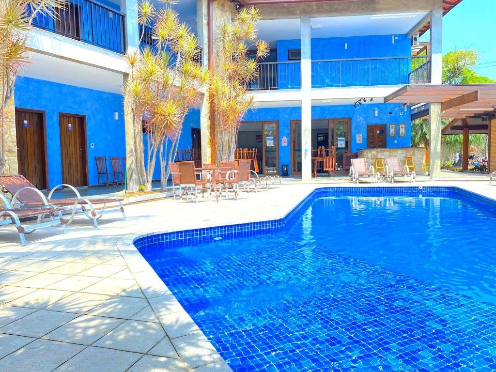 Piscina na Pousada NAAN Lázaro Ubatuba, uma piscina ampla cercada por cadeiras e mesas, ao redor também é possível enxergar as sacadas dos chalés