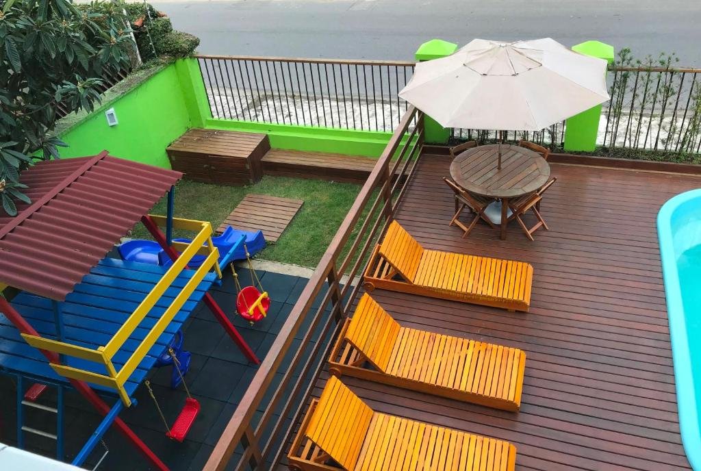 Área de recreação da POUSADA NOSSO LAR com uma parquinho infantil e, ao lado, um deck com espreguiçadeiras e uma piscina