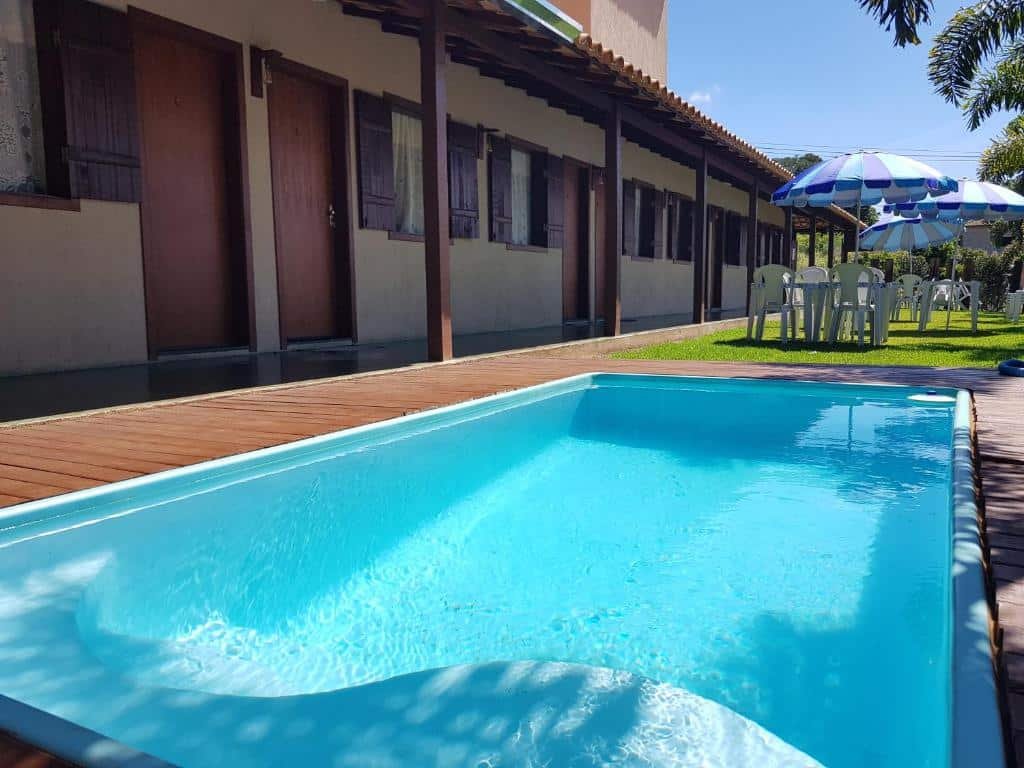Piscina na Pousada Paraíso Mineiro, com um gramado, mesas, cadeiras e guarda-sóis e, do lado esquerdo, a pousada