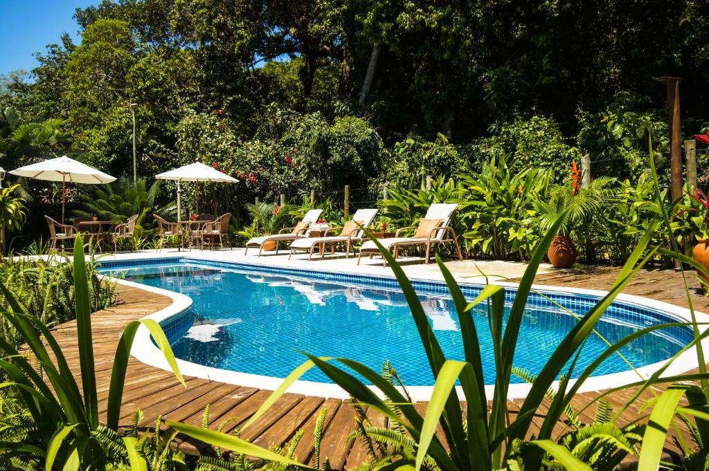 Piscina da Pousada Samambaia durante o dia com cadeiras do lado esquerdo com jardim em volta. Representa resorts em Trancoso.
