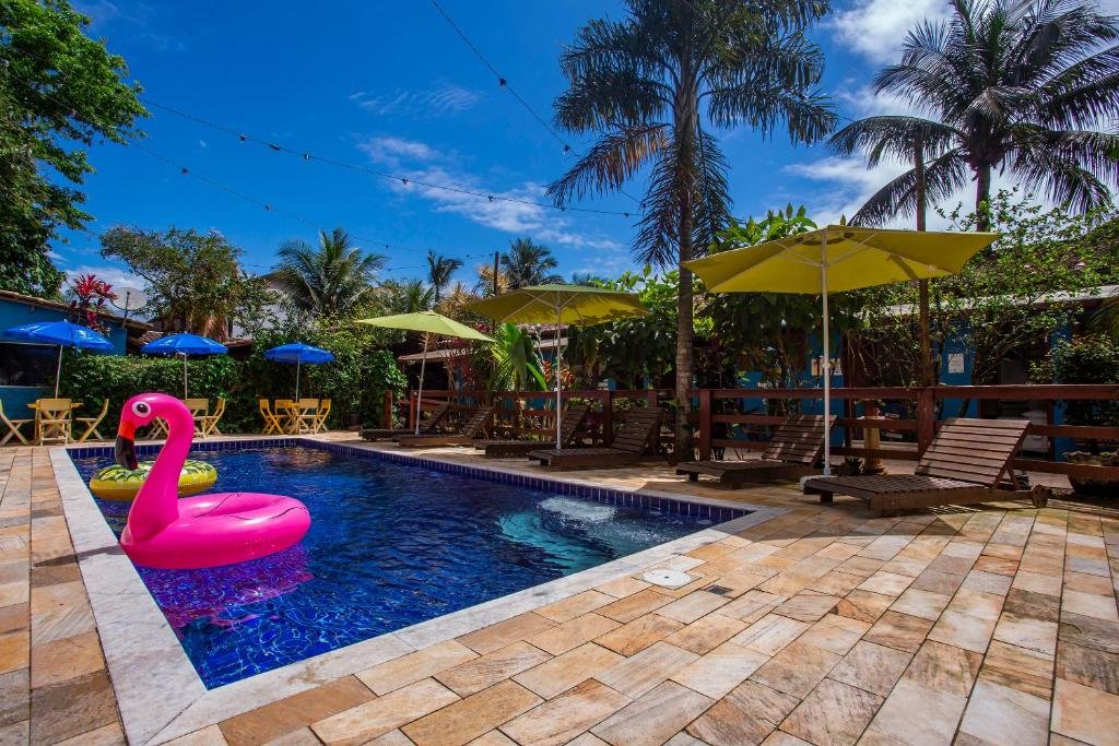 Vista da piscina da Villa Blu Maresias durante o dia, com cadeiras em volta dela, duas boias na piscina e ao fundo das cadeiras árvores e a hospedagem.