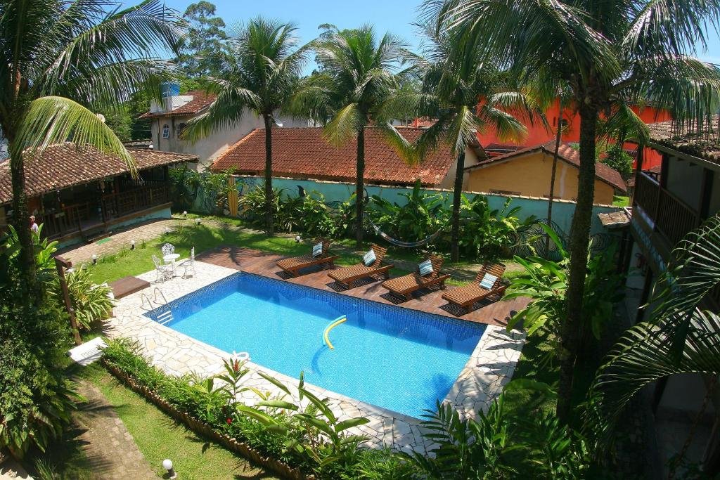 Vista de cima piscina da Pousada Tubes Maresias com cadeiras do lado esquerdo em volta de árvores e jardim.