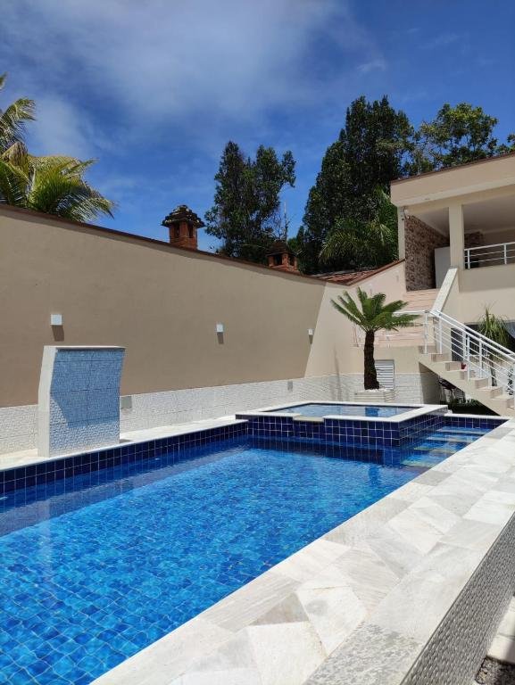 Área da piscina do Recanto da Ivete durante o dia com piscina ao centro da imagem e ao fundo a estadia.