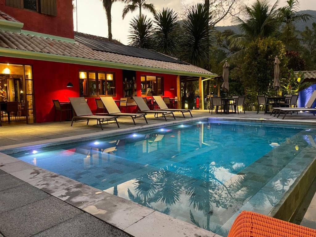 Vista da piscina da Pousada Refúgio de Maresias ,durante a noite com cadeiras do lado esquerdo perto da piscina. Representa pousadas na praia de Santiago.