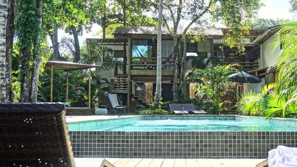 Piscina do Soleluna Casa Pousada durante o dia com cadeiras em volta e ao fundo a hospedagem. Representa resorts em Trancoso.