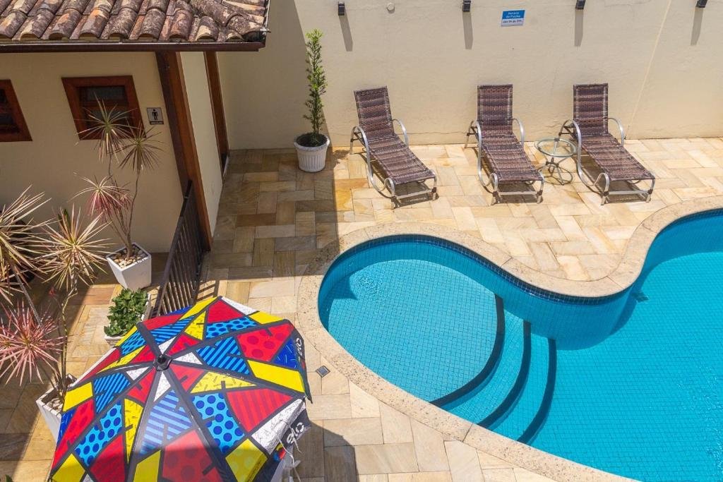 Piscina do Suítes Trilha do Sol, com uma guarda-sol colorido e três espreguiçadeiras ao redor