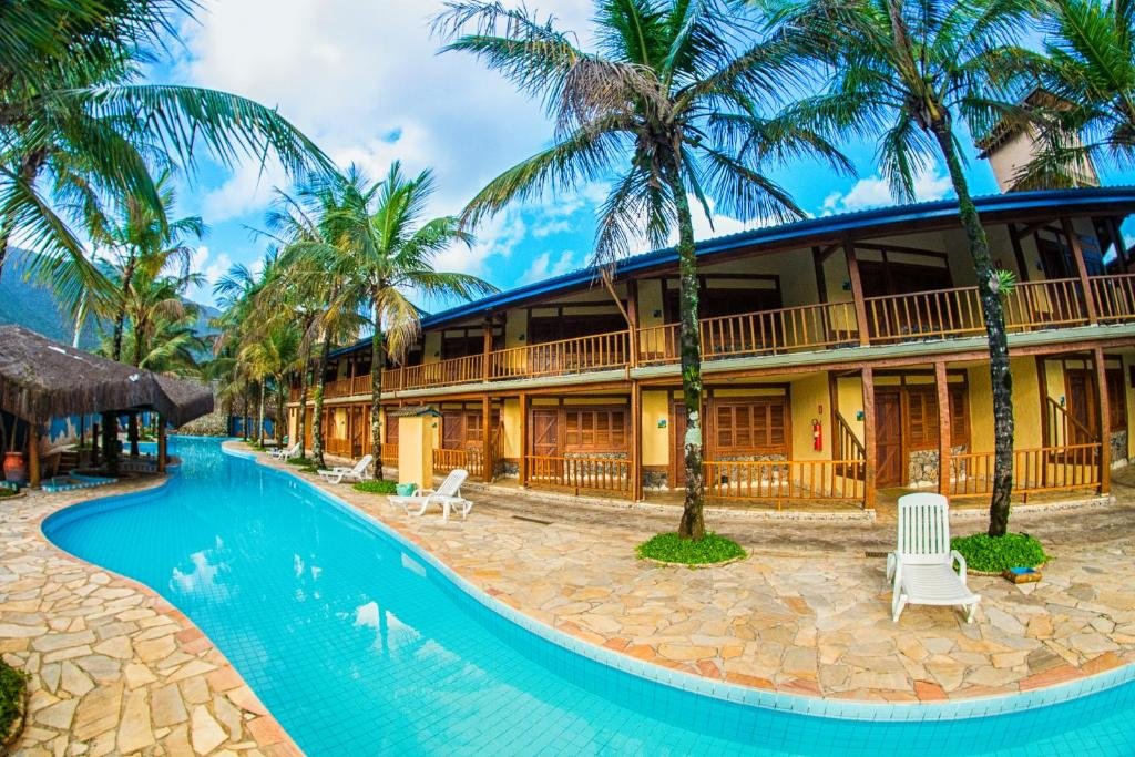 Vista da piscina da Pousada Tambayba durante o dia com cadeiras perto da piscina e ao fundo a hospedagem. Representa pousadas na praia de Santiago.