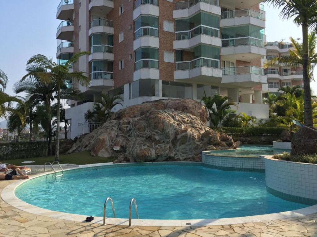 Piscina e prédio do UBATUBA, APARTAMENTO TOP, uma pedra e algumas árvores ficam próximas da piscina