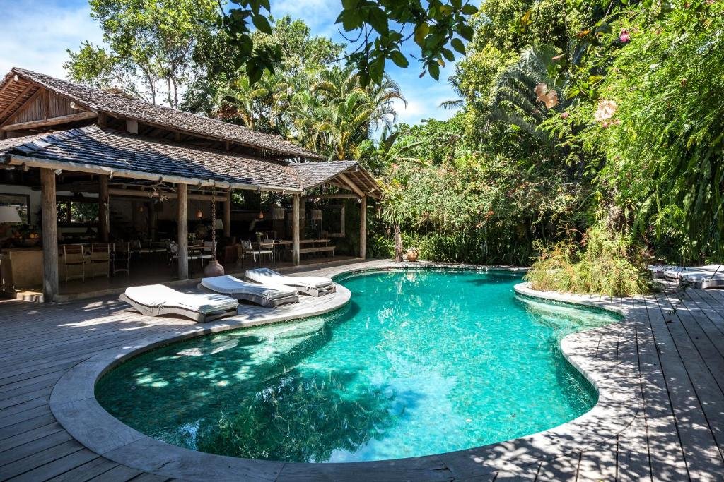Piscina do Uxua Casa Hotel & Spa, durante o dia, com cadeiras à beira da piscina do lado esquerdo e ao fundo a hospedagem. Representa resorts em Trancoso.