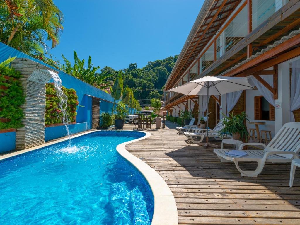 Vista da piscina da Pousada Vila Barequeçaba durante o dia com cadeiras perto da borda e ao fundo a hospedagem. Representa pousadas na praia de Guaecá.
