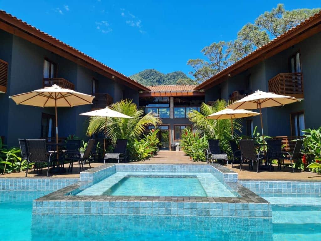 Vista da piscina da Pousada Vila Ipuan com cadeiras perto da borda da piscina e ao fundo a hospedagem. Representa airbnb na praia de Santiago.