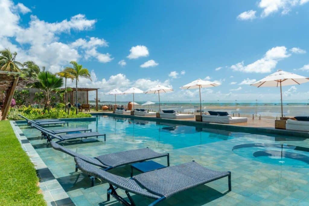 Piscina do Villa Pantai Boutique Hotel, com espreguiçadeiras na parte rasa e, mais a frente, tem colchões num deck de madeira com vista o mar bem a frente