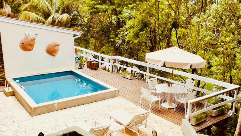 Vista da piscina do Village Toque Toque com mesas e cadeiras brancas 
 do lado esquerdo. Representa pousadas na praia de Calhetas.