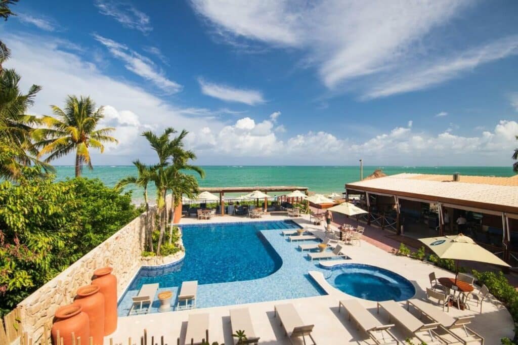 Área externa da piscina do Árvo Boutique Hotel, com espreguiçadeiras em volta, guarda-sóis e o mar ao fundo