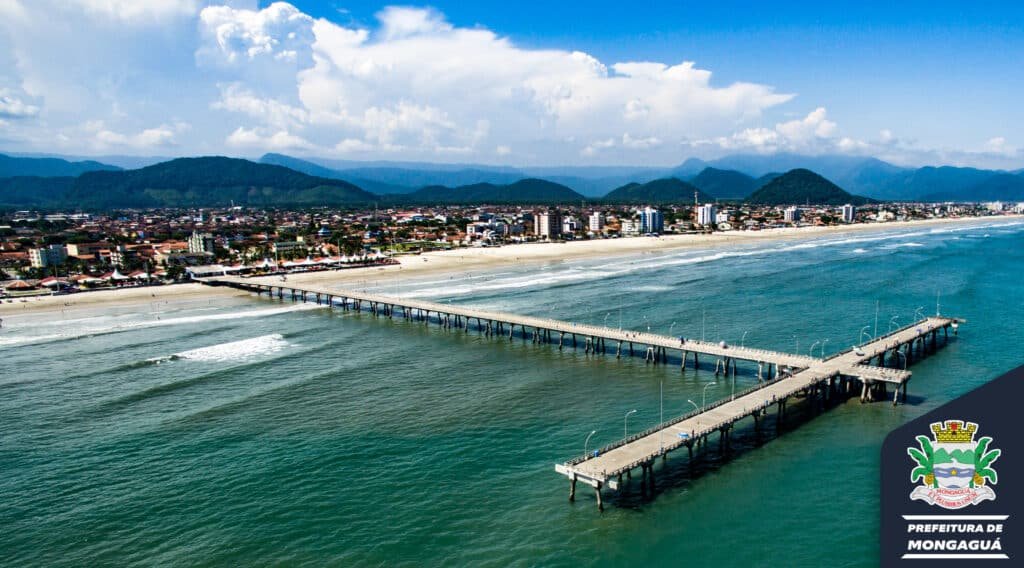 Enorme Plataforma Marítima de Pesca com praia, prédios e montanhas ao fundo. Imagem para ilustrar o post pousadas em Mongaguá.
