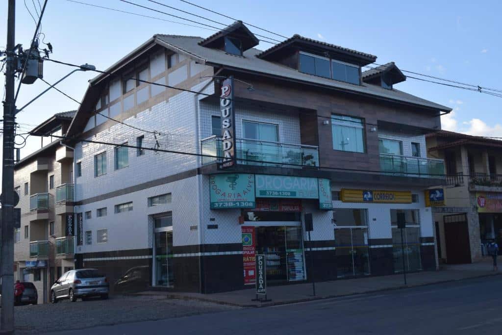 Pousada Alves em São Brás do Suaçuí, perto de Congonhas, construída em uma casa mais antiga, com azulejos quadriculados brancos e detalhes em marrom. Na parte de cima da construção há uma placa na vertical escrito "pousada" e logo atrás há uma varanda. Embaixo, há duas placas distintas. Uma verde, escrito "Drogaria" e uma amarela, escrito "correios".