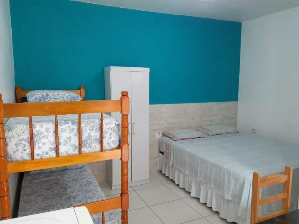 Quarto da acomodação Ancoradouro. Na parede do lado direito está uma cama de casal. Já na parede do lado esquerdo há uma beliche de duas camas. No meio delas está uma armário. 