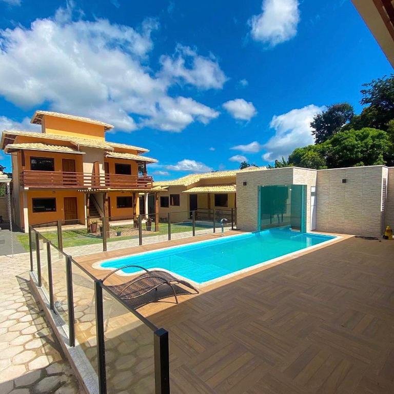 área da piscina da pousada cipó cana com uma espreguiçadeira solitária e, ao fundo, a construção amarela em dois andares da pousada.