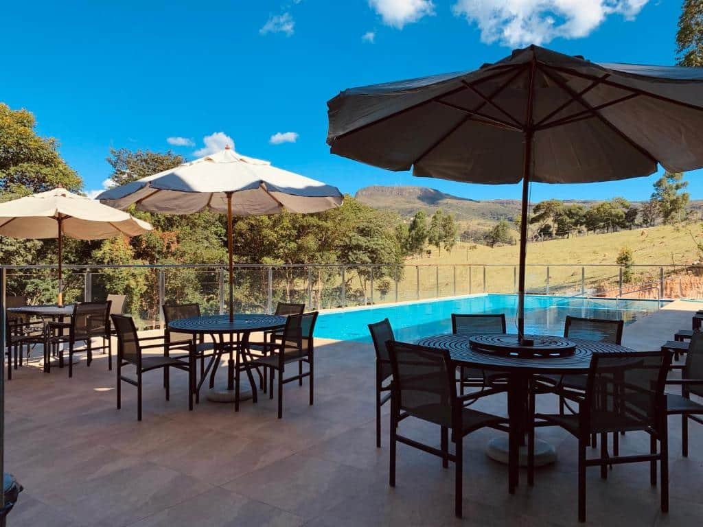 Piscina da Pousada do Batata com vista para as montanhas e, ao redor, algumas mesas com cadeiras e guarda-sóis