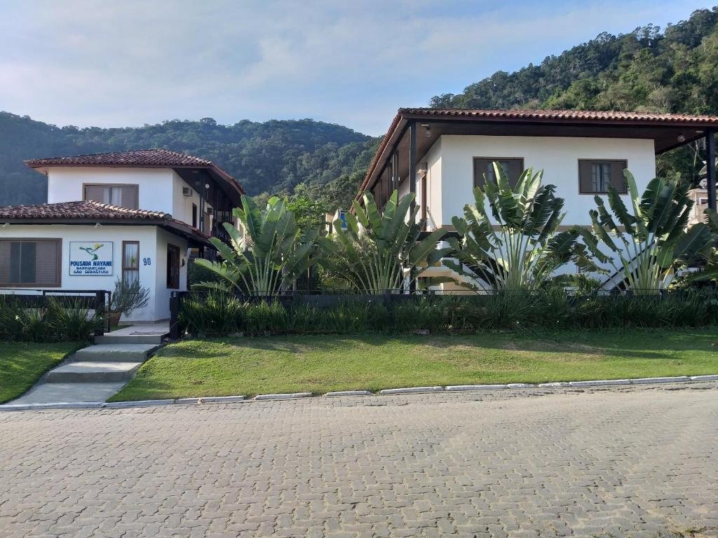 entrada da pousada nayane na praia de barequeçaba com um belo gramado na calçada e um paisagismo com plantas grandes no muro