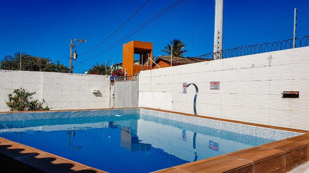 Piscina da Pousada Paraiso de Arempebe. Uma piscina no meio, no lado direito uma cascata, ao redor um muro e no fundo o portão da pousada.