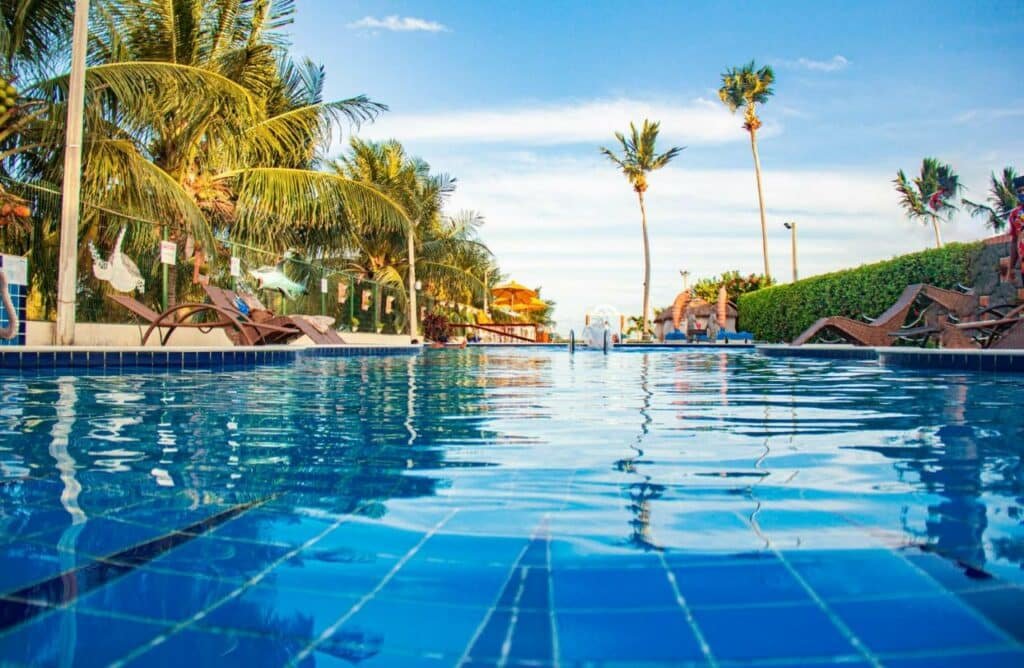 Piscina da Pousada Polymar, uma das opções de hotéis em Maragogi, aparendo a água da piscina, espreguiçadeiras e árvores em volta