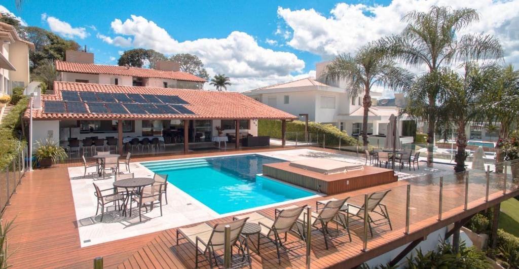Pousada Suítes do Lago, uma piscina com um deck amplo ao redor com espreguiçadeiras, cadeiras e mesas, com a pousada logo ao fundo